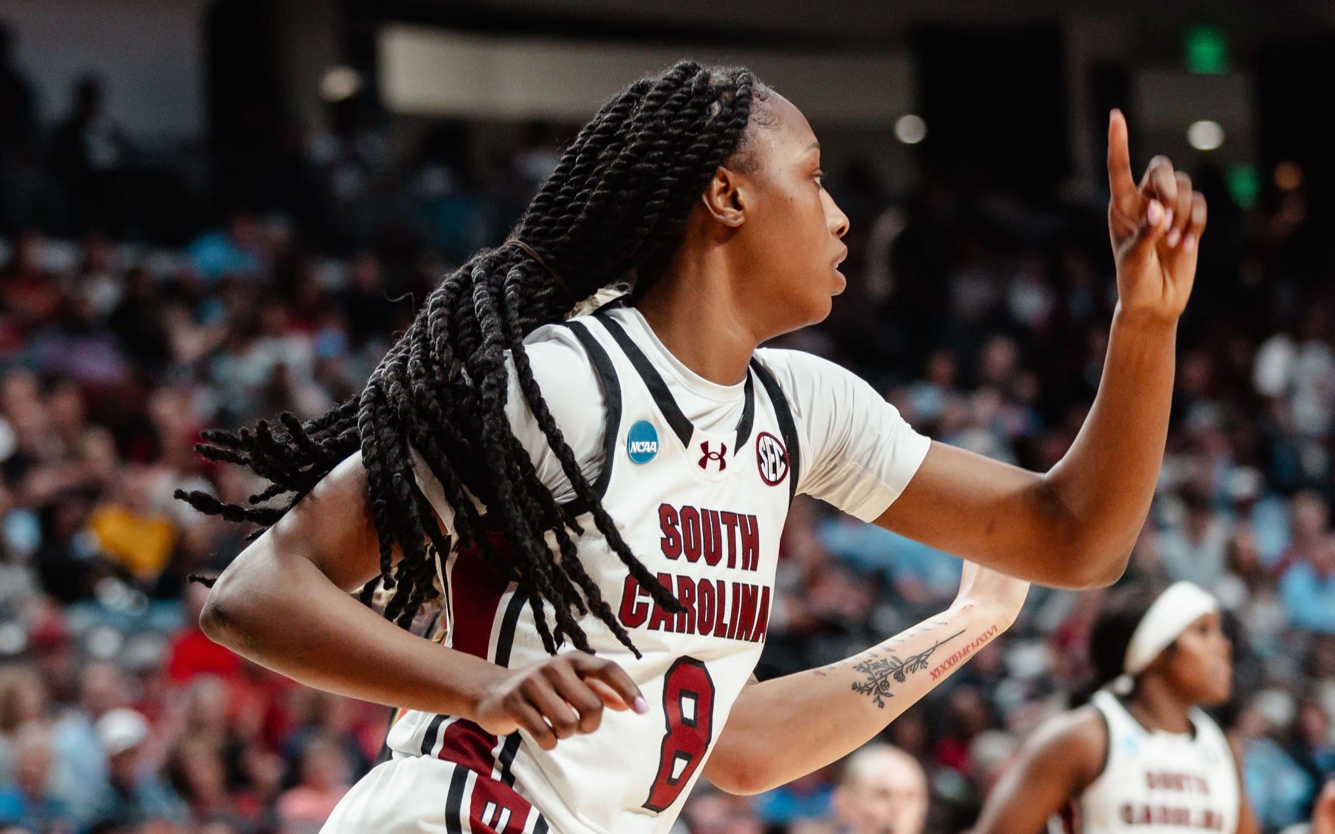 A women's basketball player holds up her finger in celebration after making a shot.